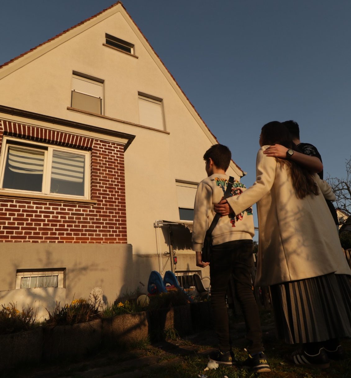Eine junge Familie steht vor einem Haus und blickt auf das Gebäude